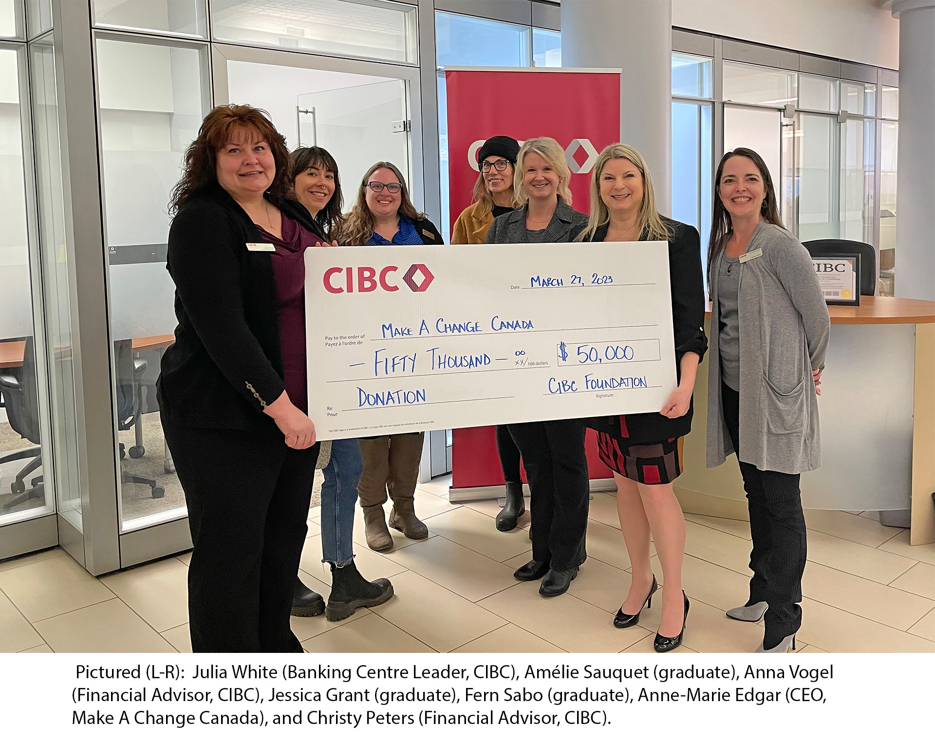 Photo of seven women standing together inside a CIBC branch with two of the women holding a large cheque written out for $50,000. Pictured from left to right: Julia White (Banking Centre Leader, CIBC), Amélie Sauquet (Graduate), Anna Vogel (Financial Advisor, CIBC), Jessica Grant (Graduate), Fern Sabo (Graduate), Anne-Marie Edgar (CEO, Make A Change Canada), and Christy Peters (Financial Advisor, CIBC).