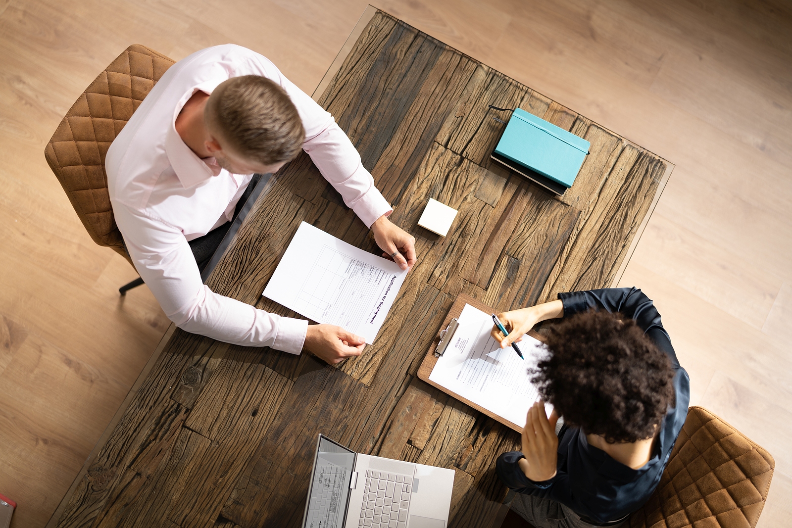 Viewed from above, a man and a woman sitting across a table from each other reading résumés.