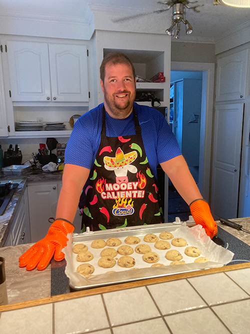 Photo of Dave in the kitchen baking, with a tray of cookies in front of him on the counter. 
