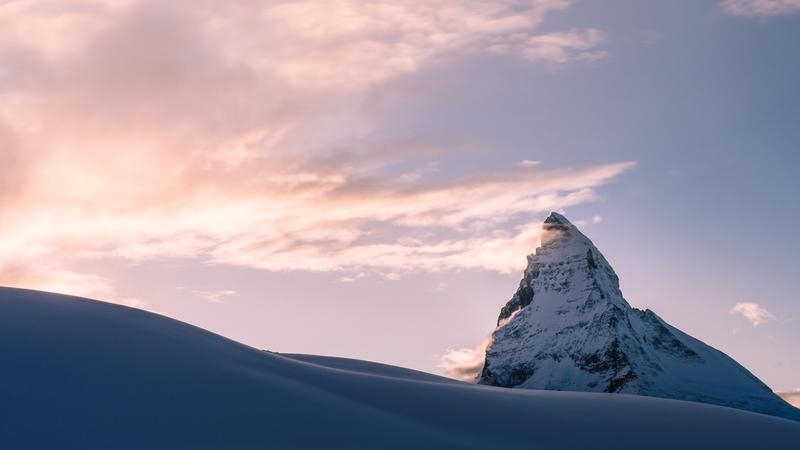 Photo of a snowy mountain peak in the foreground with a bright night sky in the background.